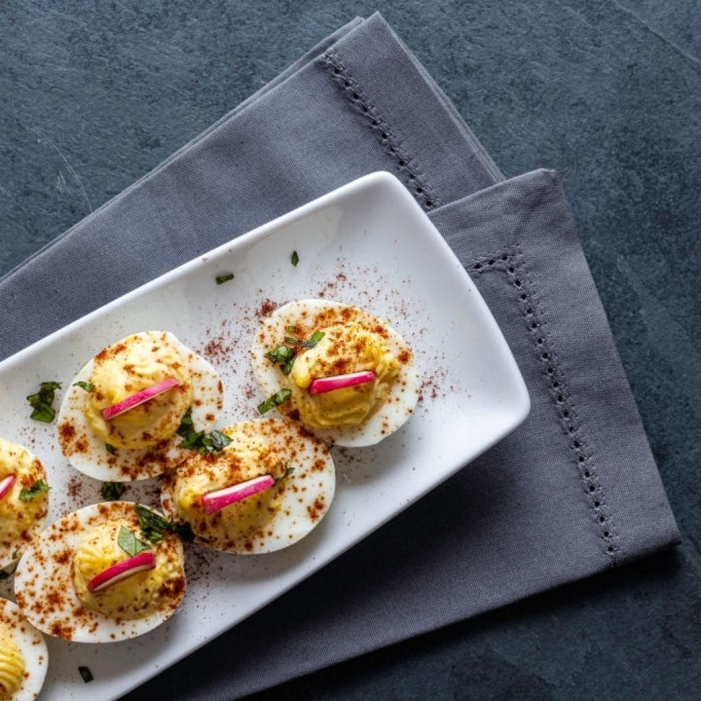 low carb deviled eggs topped with radishes, paprika and fresh basil