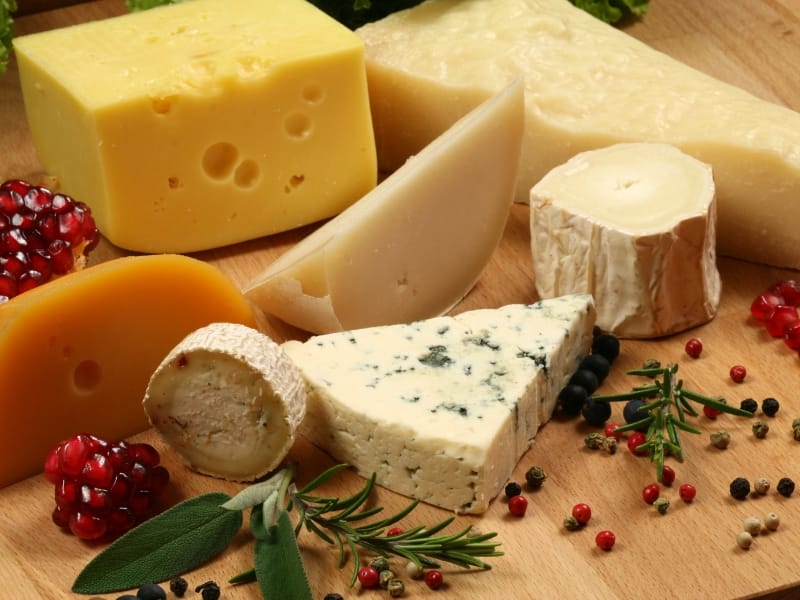 selection of cheeses including blue cheese, and swiss cheese. Surrounded by fresh pomegranetes and berries.