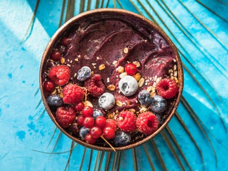 Frozen acai smoothie in coconut shell with raspberries, banana, blueberries,